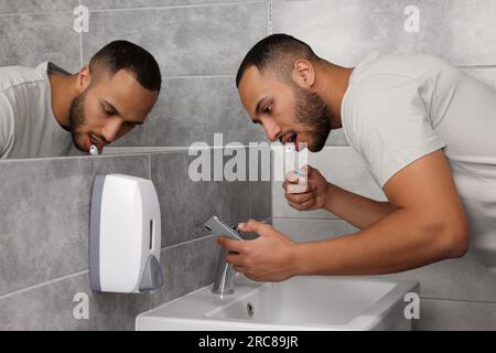 Junger Mann mit Smartphone beim Zähneputzen im Badezimmer. Internetsucht Stockfoto