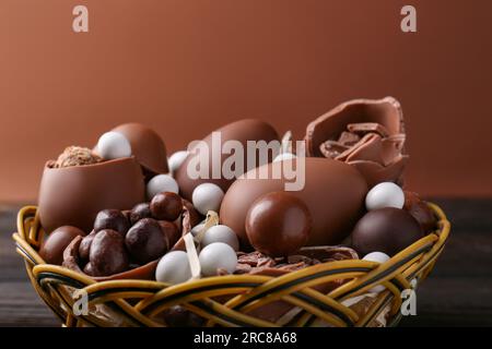 Leckere Schokoladeneier und Süßigkeiten im Korb mit Weidenkorb auf braunem Hintergrund Stockfoto