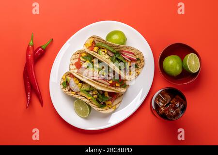 Mexikanische Küche mit Tacos mit Fleisch und gegrilltem Gemüse und Cola. Flach über Rot gelegt Stockfoto