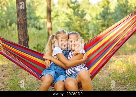 Kinder entspannen sich in einer bunten Regenbogenhängematte. Heißer Tag Garten Spaß im Freien. Mittagsschlaf während der Sommerferien. Kinder entspannen sich. Stockfoto