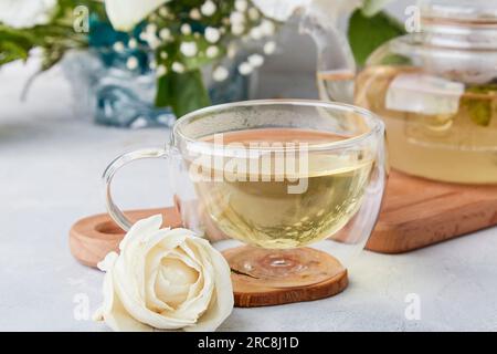 Kräuterteetasse, ästhetische Teezeit im biophilen Inneren unter weißen Blumen. Femininer, ruhiger Lebensstil, gemütliches Zuhause. Stockfoto