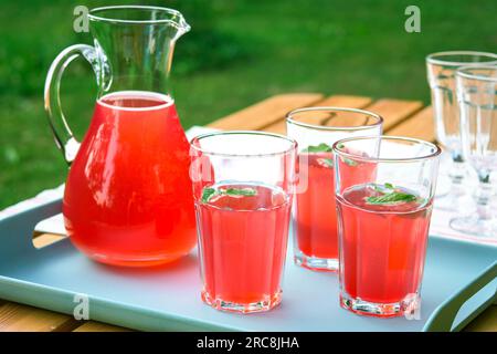 Himbeersaft in einer Kanne und Gläser im Garten. Sommergetränk für heiße Tage. Roter Fruchtsaft im Freien. Stockfoto