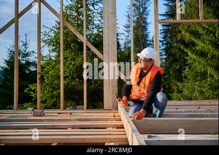 Zimmermann baut Holzrahmen. Der bärtige Mann mit Brille fährt Nägel mit einem Hammer. Dieses Projekt verkörpert die Idee des modernen, ökologisch nachhaltigen Bauens Stockfoto