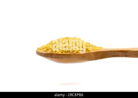 Rohbulgur-Weizen auf Holzlöffel. Stapel ungekochten trockenen Bulgur-Weizens, isoliert auf weißem Hintergrund. Schließen Stockfoto