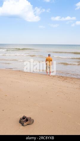 Ein Mann, der ein Bad im Meer genießt und seine Schuhe bei heißem Wetter am Strand von Horsey Beach in der Nähe von Sea Palling in einem Küstenresort in norfolk zurücklässt. Stockfoto