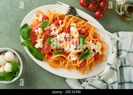 Salatcaprese oder Nudelspaghetti mit Basilikum und Mozzarella ala Caprese auf weißem Teller auf grünem rustikalem Holzhintergrund. Traditionelles italienisches Cu Stockfoto