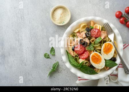 Italienischer Nudelsalat. Orekchiette-Pasta mit Thunfisch, Tomatenkirsche, Oliven, Basilikum und Parmesan auf grauem Stein- oder Betonhintergrund. Rz Stockfoto