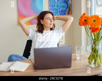 Glückliche, zufriedene latina-Frau ruht sich im Heimbüro aus, sitzt mit Laptop und hält Hände hinter dem Kopf, träumige junge Dame entspannt fertigte Arbeit, fühlt Seelenfrieden wegschauen, Traum an zukünftiges Erfolgskonzept denken Stockfoto