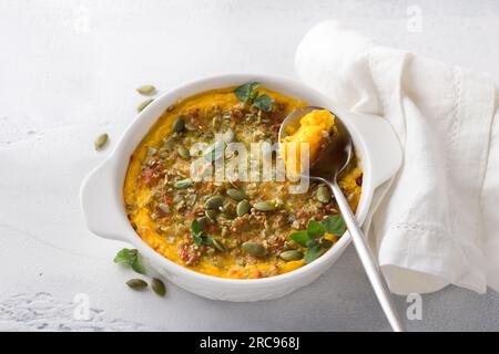 Hausgemachter Kürbisauflauf oder Gratin mit Käse und Kürbiskernen in zwei Keramikdosen auf hellgrauem Hintergrund, Draufsicht Stockfoto