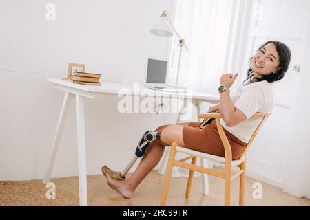 Glückliche arbeitsunfähige Frauen, die Prothesen verwenden, arbeiten gerne zu Hause. asiatische, lächelnde weibliche Prothetik. Stockfoto