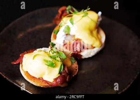 Eggs Benedict, mit Speck, garniert mit Hollandaise-Sauce und einer Garnierung. Sie werden zum Frühstück serviert. Stockfoto