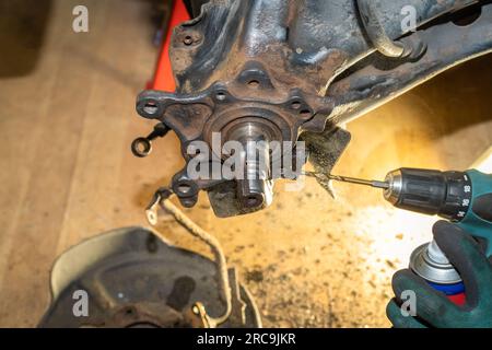 Kfz-Mechaniker repariert Radnabenlager. Beim Gewindeschneiden und Kühlen. Gelbes Licht im Hintergrund. Werkstatt. Stockfoto