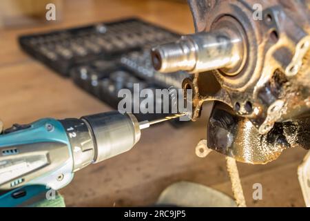 Beim Gewindedrehen entstehen Metallspäne. Der Automechaniker repariert das Nabenlager. Werkzeugkasten im Hintergrund. Gelbes Licht. Stockfoto