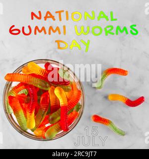 Gummi-Würmer auf weißem Marmorhintergrund mit Text: "Nationaler Gummi-Wurm-Tag. Juli 15 Stockfoto