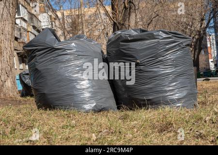 Zwei schwarze Säcke mit Müll, alte gefallene Blätter, Äste auf dem Boden. Frühjahrsputz. Straßenreinigung in der Stadt. Stockfoto