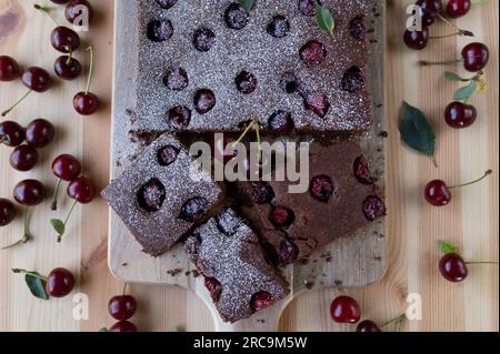 Schokoladenkuchen mit Sauerkirschen auf einem hellen Holztisch. Draufsicht Stockfoto
