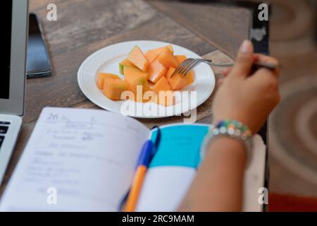 Nahaufnahme der Hand einer Frau, die gehackte Früchte von einem Teller nimmt, während sie in einem Café arbeitet Stockfoto