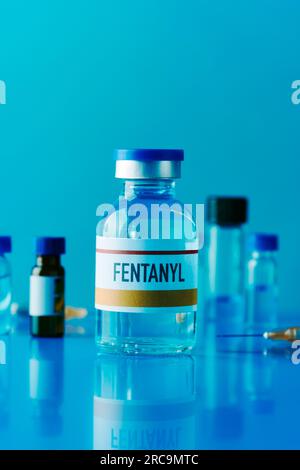 Eine Scheinflasche Fentanyl auf einem blauen Tisch neben einer Spritze und einigen anderen Durchstechflaschen Stockfoto