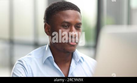 Ein rücksichtsvoller Schwarzer in einer Brille, der sich mit einer schwierigen Aufgabe auseinandersetzt, auf den Computerbildschirm schaut, an eine Problemlösung denkt Stockfoto
