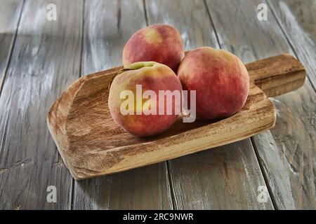 Pfirsiche liegen auf einer Holzschaufel auf grauem Holzhintergrund Stockfoto