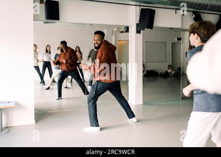 Ein lächelnder Lehrer, der Teenager ansieht, die Tanzen im Studio an der Highschool üben Stockfoto