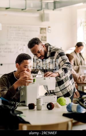 Lehrer, der dem Schüler in der Highschool die Nähmaschine erklärt Stockfoto