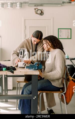 Lehrerin, die weibliche Schülerin beim Anschauen einer Nähmaschine im Kunstunterricht an der Highschool unterstützt Stockfoto