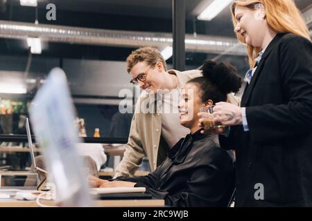 Lächelndes Multirassenteam, das über ein Notebook diskutiert, während es seine Strategie im Büro plant Stockfoto