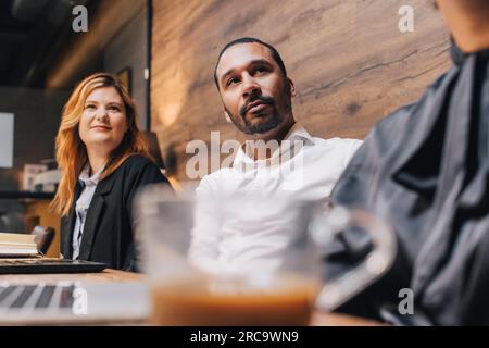 Geschäftsmann, der während der Besprechung mit weiblichen Kollegen an einem Konferenztisch im Konferenzraum sitzt Stockfoto