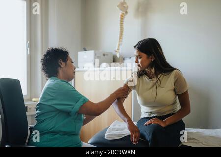 Seitenansicht einer Arztin, die den Arm einer jungen Frau während der medizinischen Untersuchung untersucht Stockfoto