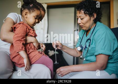 Ärztin mit Reflexhammer, die das Mädchen in der Klinik untersucht Stockfoto