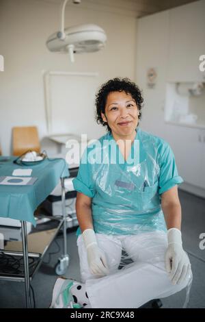 Porträt einer lächelnden Ärztin in Uniform, die im Untersuchungsraum sitzt Stockfoto