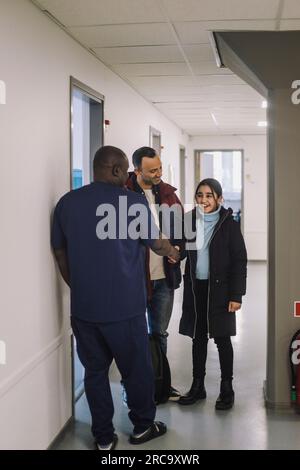 Lächelndes Mädchen, das sich die Hand schüttelt, während ein Arzt auf dem Krankenhausflur steht Stockfoto