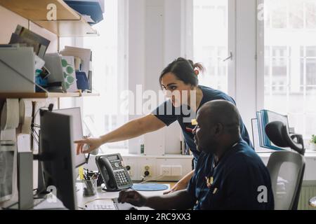 Krankenschwester zeigt über Computer, während sie mit einem Kollegen im Krankenhaus spricht Stockfoto