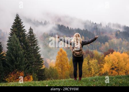 Glücklicher Tourist, der den Herbst im Wald genießt. Eine Frau nimmt das mentale Wohlbefinden der Natur während einer Bergwanderung mit Stockfoto