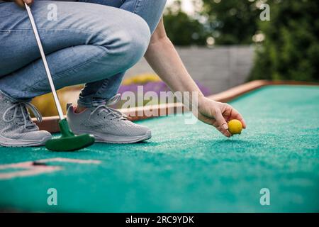 Frau, die draußen Minigolf auf grünem Kunstrasen spielt. Sommerfreizeitaktivitäten Stockfoto