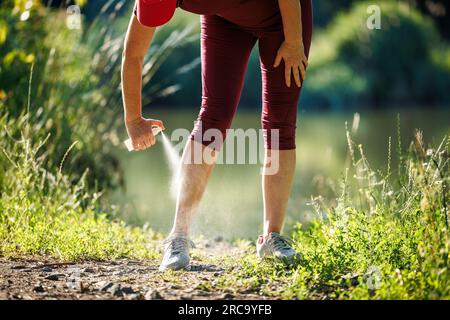 Frau, die Insektenschutzmittel gegen Mücken aufträgt und Zecken auf ihrem Bein aufträgt, bevor sie im Freien joggt Stockfoto