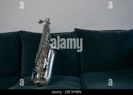 Silbernes Baritonsaxofon, auf dem Sofa im Wohnzimmer zu Hause, Kopierraum, Musikinstrumentkonzept. Stockfoto