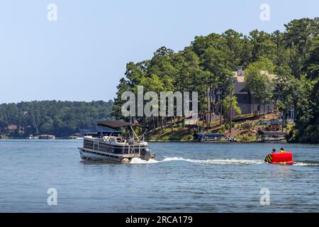 Ein Pontonboot, das aufblasbare Schlauchfloß auf dem See zieht. Familie auf einem Pontonpartyboot, die an einem Sommertag mit ihren Kindern Tubing genießt. Stockfoto