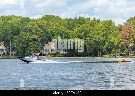 Motorboot zieht aufblasbares Schlauchboot auf dem See. Eine Familie auf einem Skiboot, die an einem Sommertag mit ihren Kindern Tubing genießt. Stockfoto