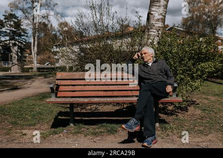 Seniorenmann, der an sonnigen Tagen auf einer Bank im Park sitzt Stockfoto