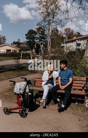 Seniorin spricht mit männlichem Betreuer, während sie auf der Bank sitzt Stockfoto