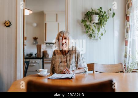 Porträt einer glücklichen Seniorin, die zu Hause am Esstisch sitzt Stockfoto