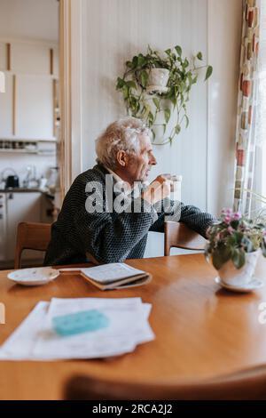 Seniorenmann trinkt Tee, während er zu Hause am Esstisch sitzt Stockfoto