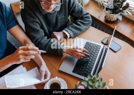 Blick aus dem hohen Blickwinkel auf einen älteren Mann, der ein Notebook mit einem pflegenden Mann zu Hause benutzt Stockfoto