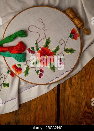 Blumenstickerei auf weißem Textil mit Korbholz-Hintergrund. Traditionelle stickereien mit stickerei aus ukrainischer Zahnseide. Handgemachte Kleidung aus ethnischer Herkunft, Handtuchhalter Stockfoto