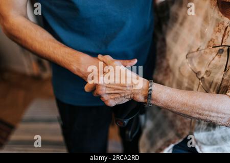 Mittelteil des männlichen Gesundheitspersonals, der die Hand einer älteren Frau zu Hause hält Stockfoto