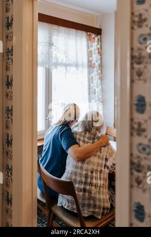 Pflegehelferin sitzt mit Seniorin zu Hause auf dem Stuhl Stockfoto