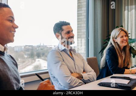 Lächelnder Geschäftsmann mit gekreuzten Armen während des Meetings in einer Arbeitsstelle Stockfoto
