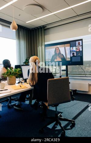 Männliche und weibliche Kollegen, die Videoanrufe mit Geschäftsfrau im Fernsehen in einer Arbeitsstelle führen Stockfoto